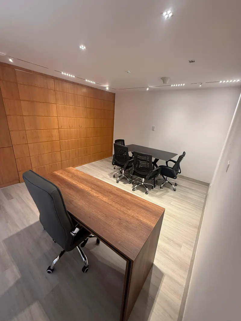 Despacho con escritorio de madera y sala de reuniones al fondo