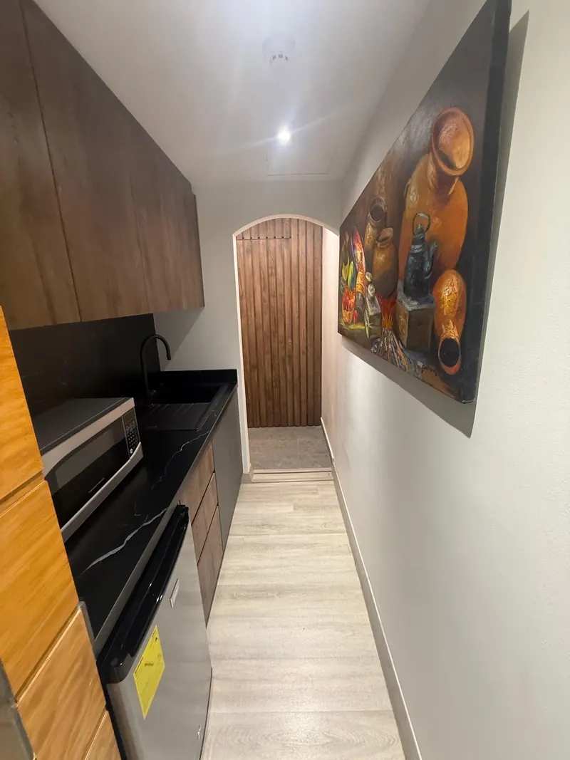Cocina de la oficina con muebles de madera y pasillo hacia una puerta en arco